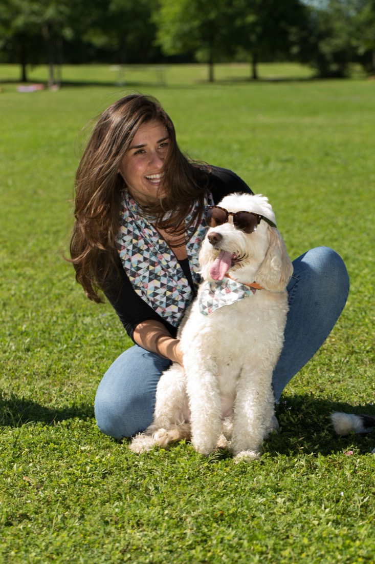 Nicole sitting in the grass with her white doodle, who is wearing sunglasses